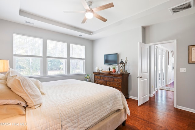 bedroom with dark hardwood / wood-style floors, ceiling fan, a raised ceiling, and multiple windows