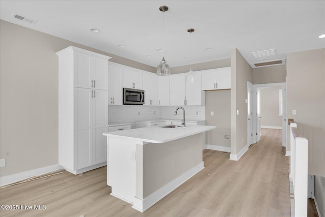 822 Kenneth Ave Unit 1, Carolina Beach, NC 28428 - kitchen with stainless steel microwave, light wood-style flooring, tasteful backsplash, white cabinetry, and a kitchen island with sink