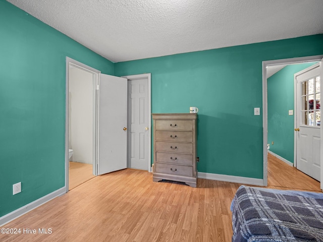 bedroom with light hardwood / wood-style floors, a textured ceiling, and ensuite bath