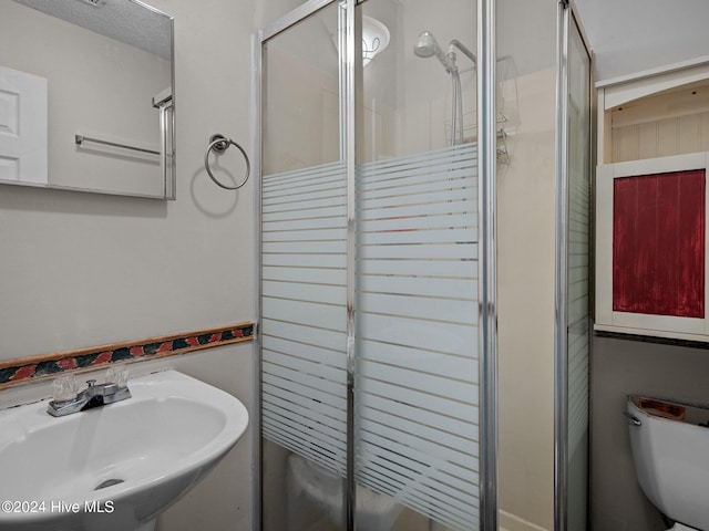 bathroom featuring toilet, a shower with door, and sink