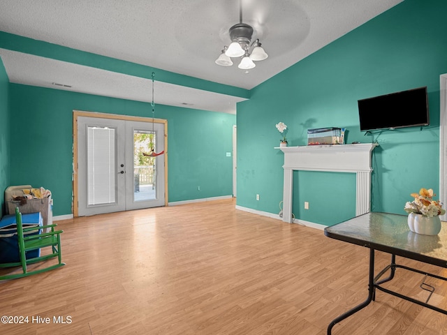 living room featuring ceiling fan, french doors, a textured ceiling, and light hardwood / wood-style flooring