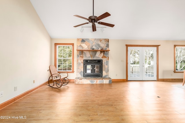 unfurnished living room featuring ceiling fan, french doors, a stone fireplace, light hardwood / wood-style flooring, and vaulted ceiling