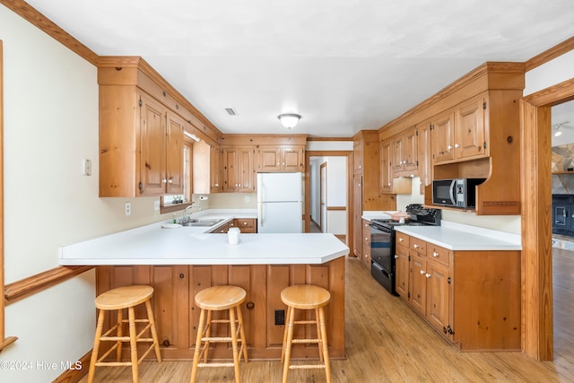 kitchen featuring a kitchen bar, kitchen peninsula, light wood-type flooring, sink, and black appliances