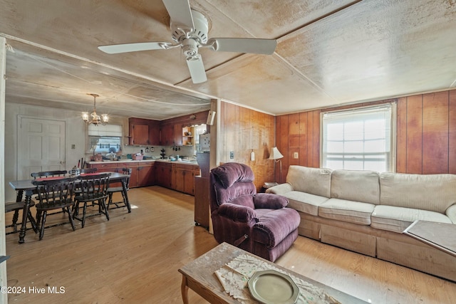 living room with ceiling fan with notable chandelier, light hardwood / wood-style floors, and wooden walls