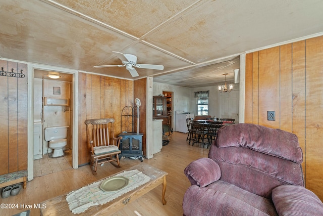 living room with a wood stove, wooden walls, wood-type flooring, and ceiling fan with notable chandelier