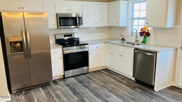 kitchen with light stone counters, stainless steel appliances, dark wood-type flooring, sink, and white cabinets