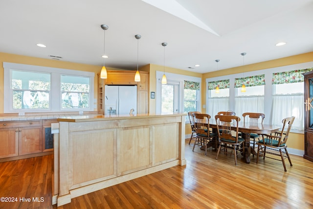 kitchen with hanging light fixtures, light hardwood / wood-style flooring, plenty of natural light, and white fridge with ice dispenser