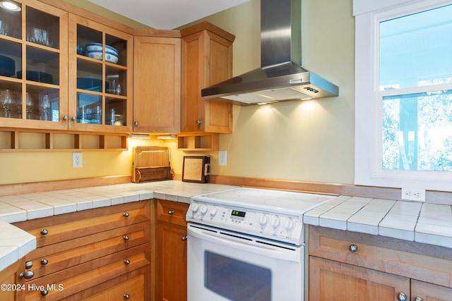 kitchen featuring white stove, tile countertops, and wall chimney range hood