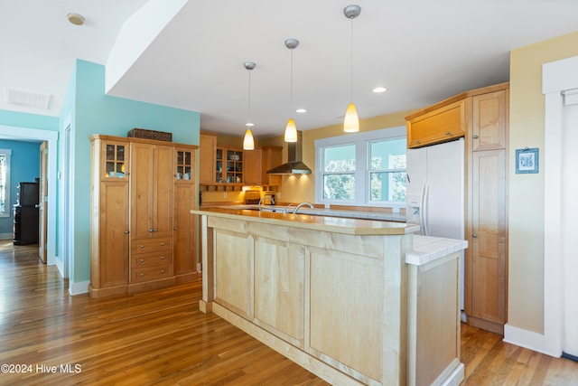 kitchen with a center island, wall chimney range hood, light hardwood / wood-style flooring, white fridge with ice dispenser, and decorative light fixtures