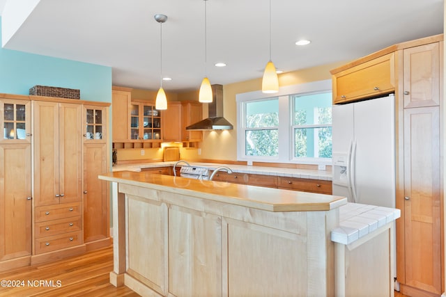 kitchen featuring white refrigerator with ice dispenser, light brown cabinetry, light hardwood / wood-style flooring, and wall chimney range hood