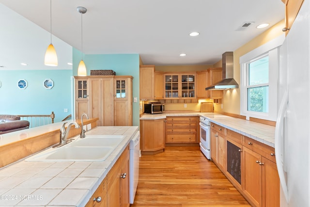 kitchen featuring white appliances, sink, wall chimney range hood, tile countertops, and light hardwood / wood-style floors