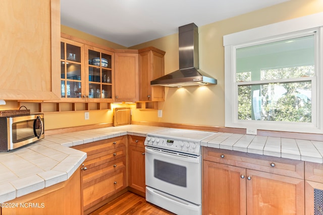 kitchen featuring tile counters, white electric range oven, wall chimney range hood, and wood-type flooring