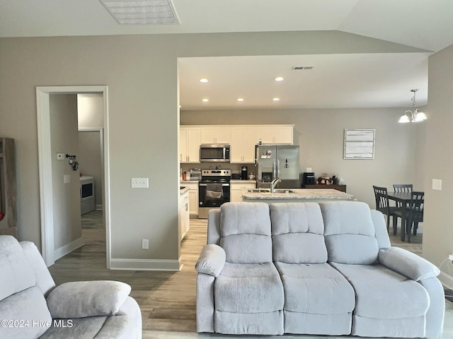 living room with a notable chandelier, lofted ceiling, sink, and light hardwood / wood-style flooring