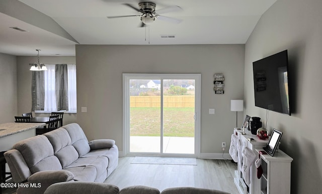 living room with ceiling fan with notable chandelier, light hardwood / wood-style floors, and vaulted ceiling