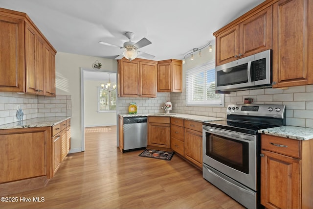 kitchen with ceiling fan with notable chandelier, light wood-type flooring, stainless steel appliances, and light stone counters