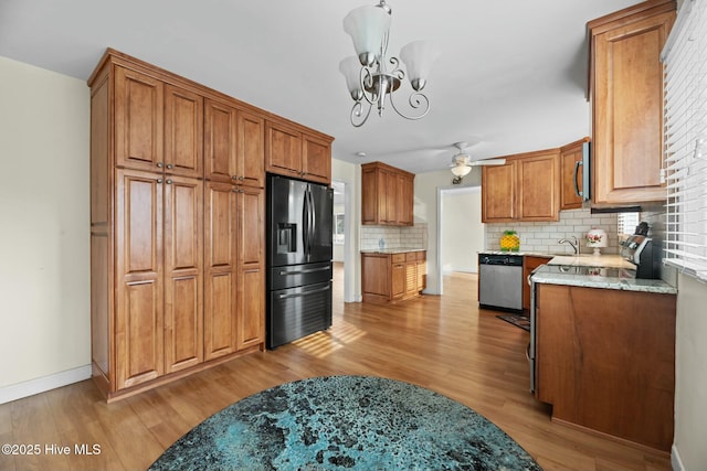 kitchen with ceiling fan with notable chandelier, light stone countertops, light wood-type flooring, appliances with stainless steel finishes, and tasteful backsplash