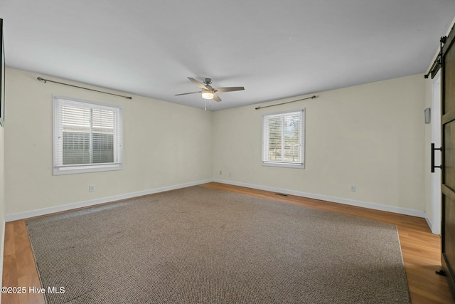 spare room featuring a barn door, ceiling fan, light hardwood / wood-style flooring, and a healthy amount of sunlight