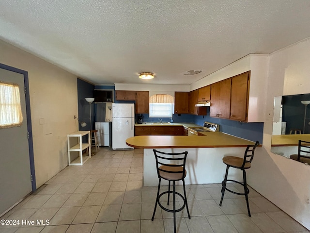 kitchen with electric stove, sink, white fridge, kitchen peninsula, and a breakfast bar area