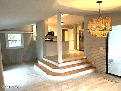 interior space with hardwood / wood-style flooring, a notable chandelier, brick wall, and vaulted ceiling