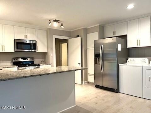 kitchen with kitchen peninsula, appliances with stainless steel finishes, light stone counters, independent washer and dryer, and white cabinetry