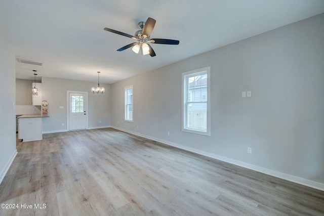 unfurnished living room featuring ceiling fan with notable chandelier, a healthy amount of sunlight, and light hardwood / wood-style flooring