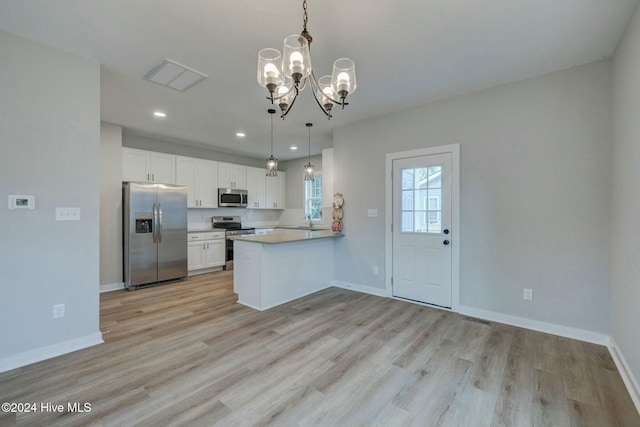 kitchen featuring an inviting chandelier, kitchen peninsula, decorative light fixtures, white cabinets, and appliances with stainless steel finishes