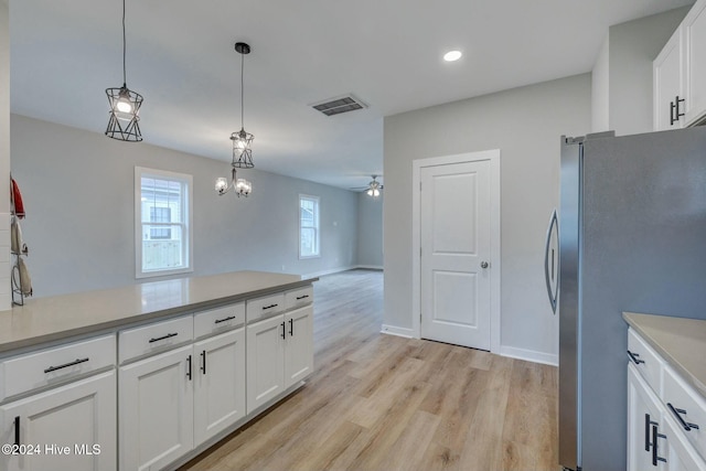 kitchen featuring pendant lighting, ceiling fan with notable chandelier, light hardwood / wood-style flooring, white cabinetry, and stainless steel refrigerator