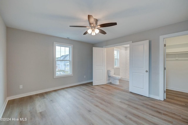 unfurnished bedroom featuring connected bathroom, ceiling fan, a walk in closet, a closet, and light wood-type flooring