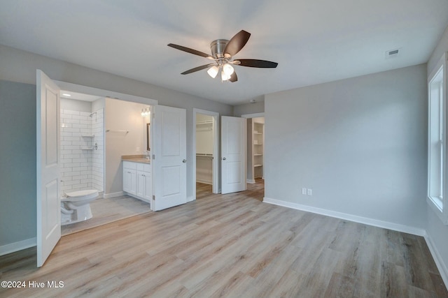 unfurnished bedroom featuring ceiling fan, a spacious closet, connected bathroom, light hardwood / wood-style floors, and a closet