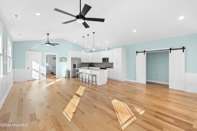 kitchen featuring a kitchen bar, decorative light fixtures, appliances with stainless steel finishes, a barn door, and a kitchen island with sink