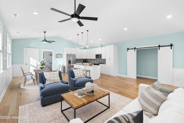 living room featuring vaulted ceiling, a barn door, sink, and light hardwood / wood-style floors