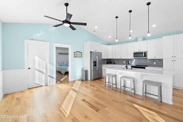 kitchen with a breakfast bar area, white cabinetry, appliances with stainless steel finishes, an island with sink, and pendant lighting