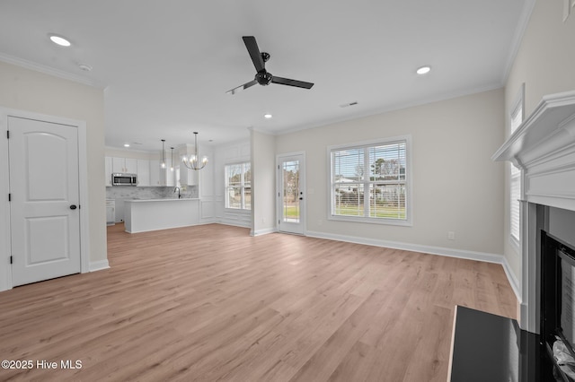 unfurnished living room with baseboards, crown molding, light wood-type flooring, a fireplace, and ceiling fan with notable chandelier