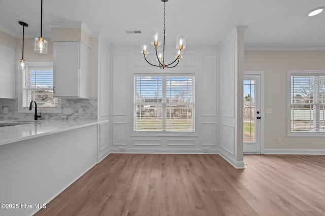 unfurnished dining area with crown molding, a sink, visible vents, and a decorative wall