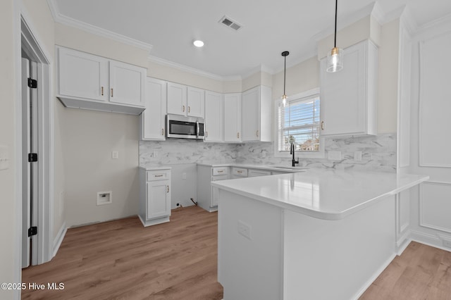 kitchen with light wood finished floors, stainless steel microwave, white cabinetry, a sink, and a peninsula