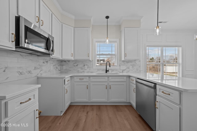 kitchen featuring stainless steel appliances, a peninsula, a sink, visible vents, and crown molding