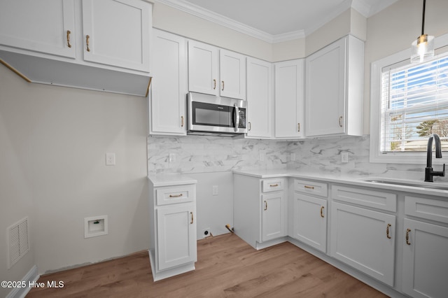 kitchen featuring decorative backsplash, stainless steel microwave, light countertops, crown molding, and a sink