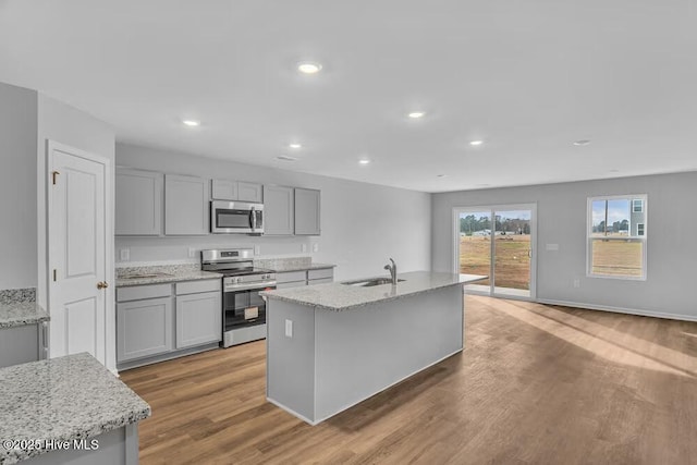 kitchen featuring a kitchen island with sink, sink, light stone counters, and stainless steel appliances