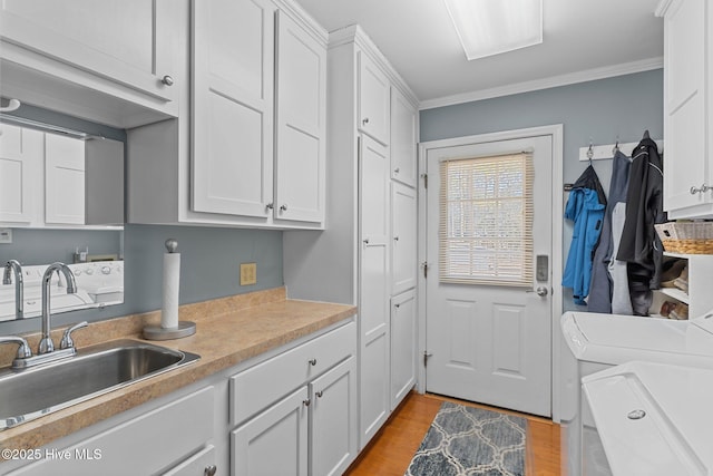 washroom featuring sink, crown molding, cabinets, light hardwood / wood-style floors, and washing machine and clothes dryer