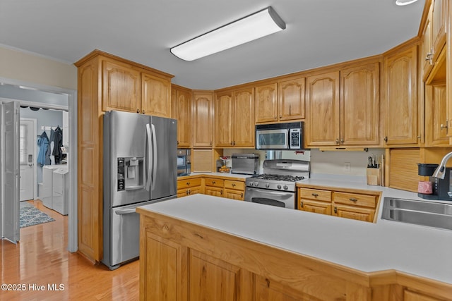 kitchen with sink, appliances with stainless steel finishes, washer and dryer, kitchen peninsula, and light wood-type flooring