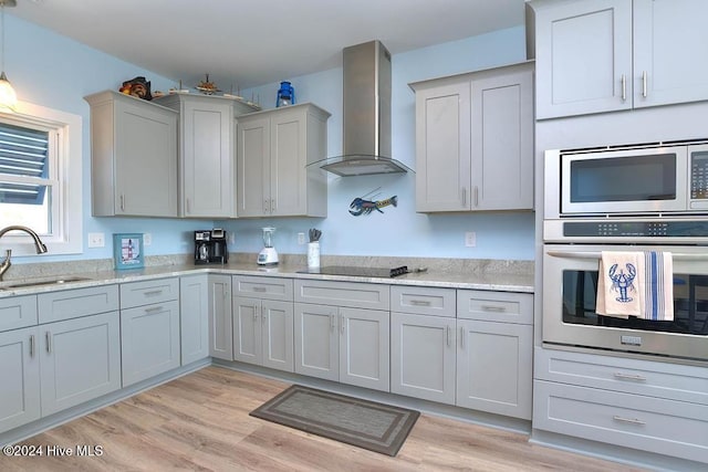 kitchen featuring sink, light hardwood / wood-style flooring, wall chimney exhaust hood, gray cabinets, and stainless steel appliances