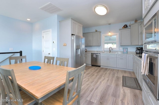 interior space featuring pendant lighting, sink, light hardwood / wood-style flooring, gray cabinets, and appliances with stainless steel finishes