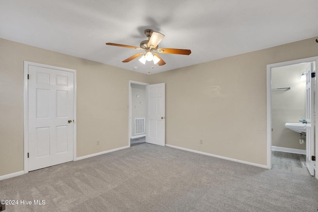 unfurnished bedroom with light carpet, a walk in closet, ensuite bath, and ceiling fan