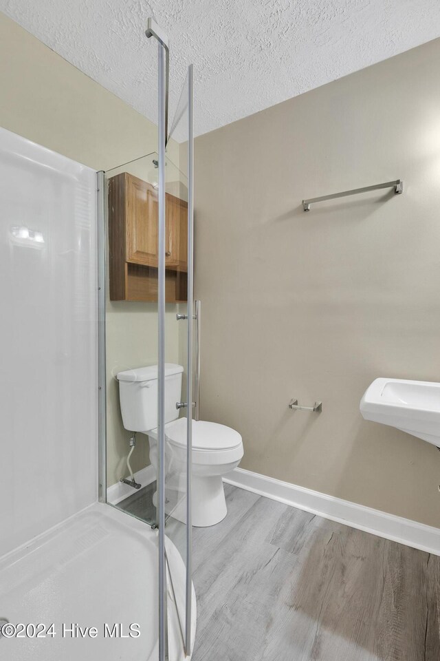 bathroom featuring wood-type flooring, a textured ceiling, toilet, and walk in shower