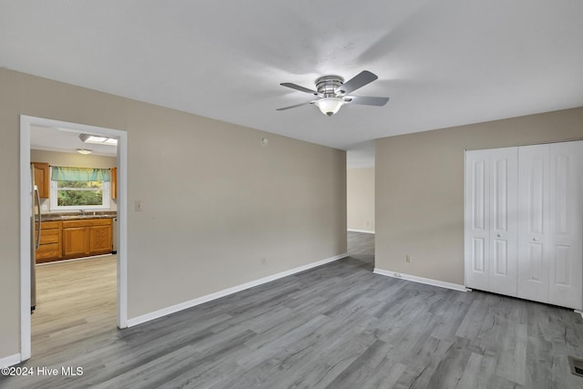 unfurnished bedroom featuring stainless steel refrigerator, ceiling fan, sink, a closet, and light wood-type flooring