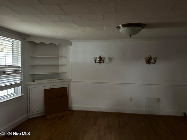 spare room with built in shelves and dark hardwood / wood-style floors