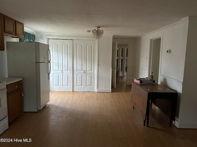 kitchen with a textured ceiling, crown molding, light hardwood / wood-style flooring, a notable chandelier, and white fridge