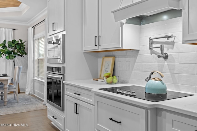 kitchen with ornamental molding, black electric cooktop, light hardwood / wood-style floors, white cabinetry, and range hood