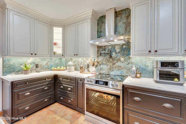 kitchen featuring backsplash, wall chimney exhaust hood, stainless steel electric stove, light tile patterned floors, and white cabinetry