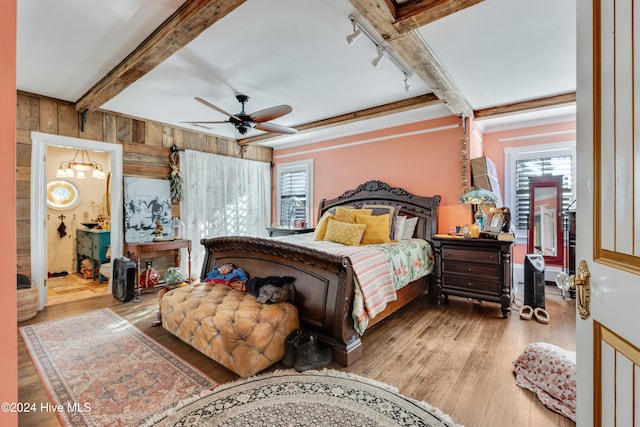 bedroom featuring connected bathroom, ceiling fan, wooden walls, and multiple windows